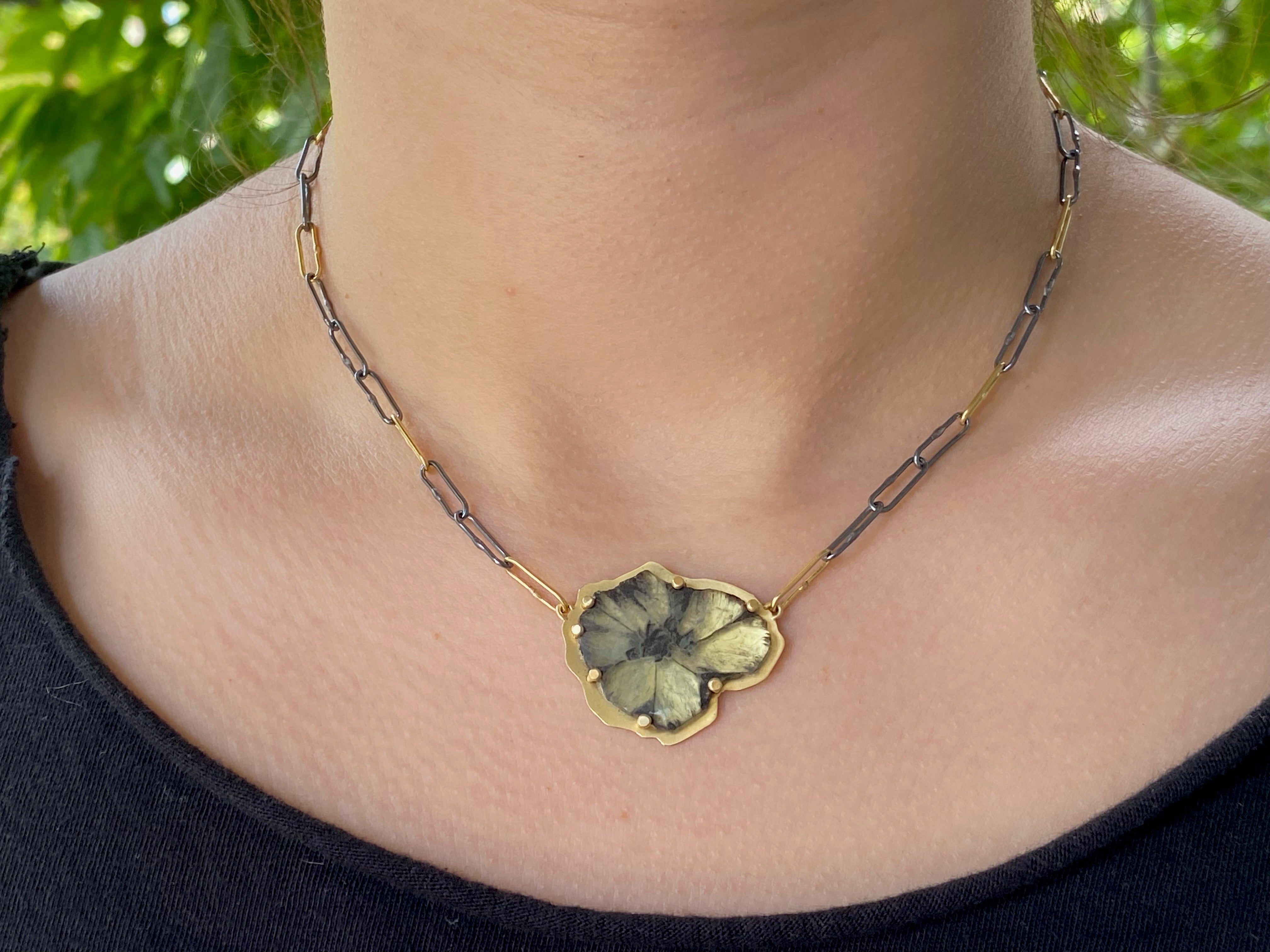 Pansy-shaped Trapiche emerald pendant set in gold, worn on a chain of oxidized silver and gold links